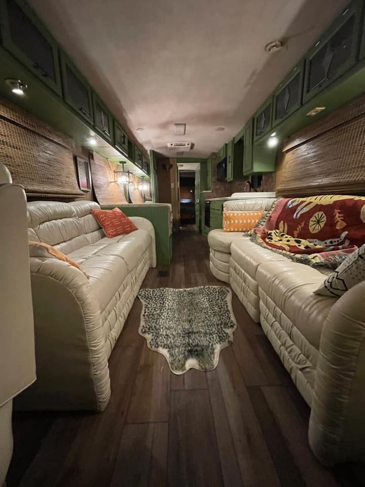 Inside a renovated RV, with cream couches, green cabinets, and dark wood floors.
