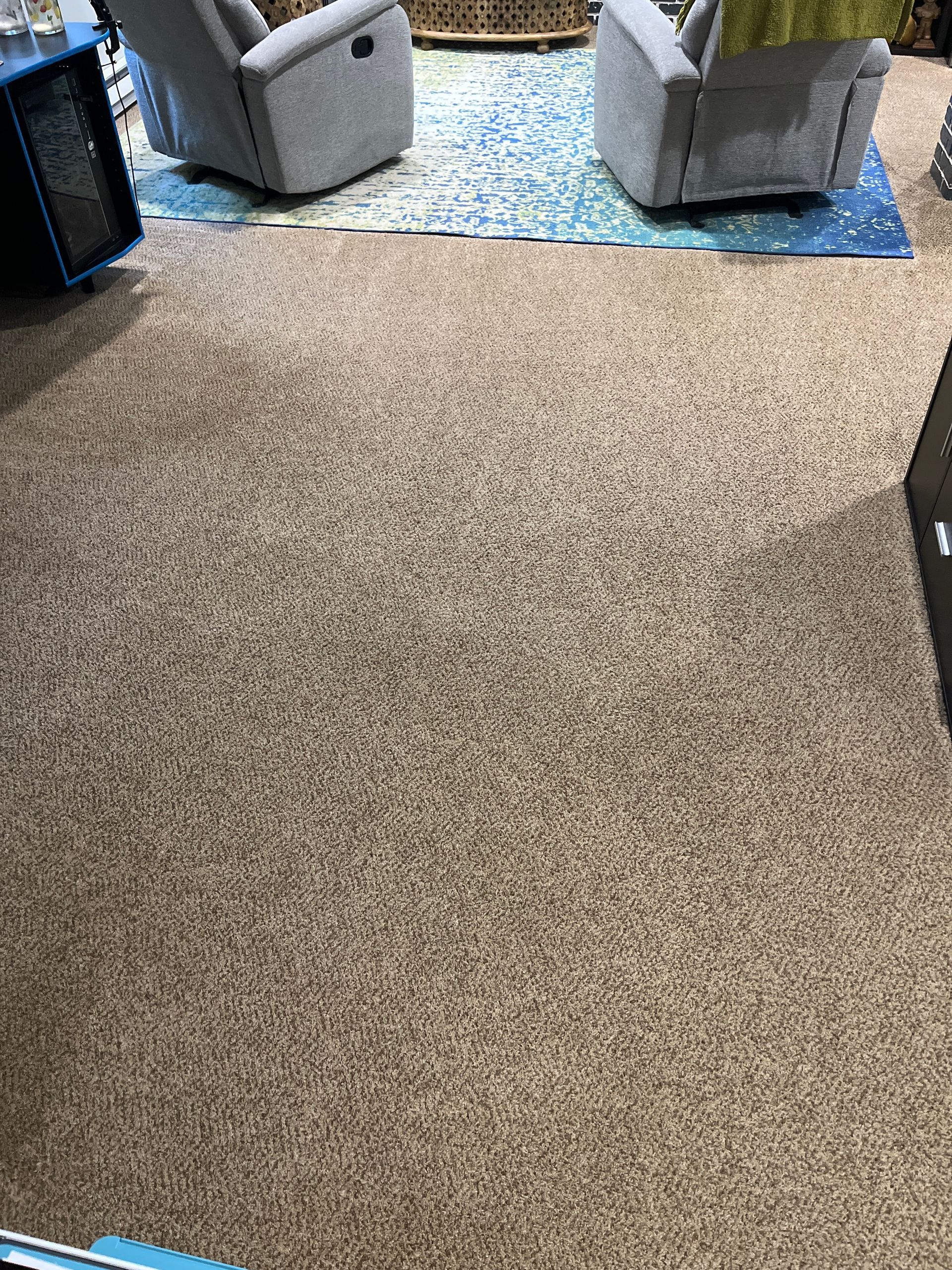 Overhead view of tan carpet in a living room, with light blue recliner chairs and a patterned rug in the background.