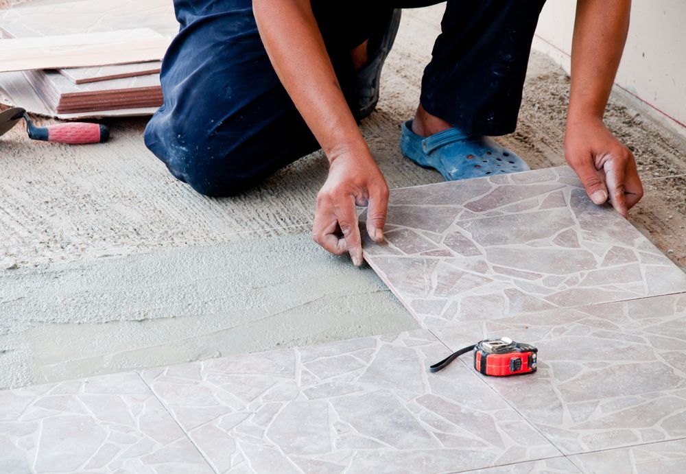 A man is kneeling down to install a tile floor.