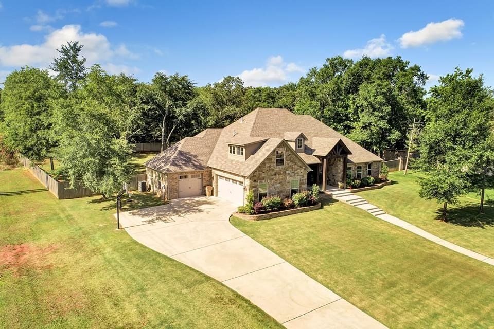 An aerial view of a large house with a driveway leading to it surrounded by trees.