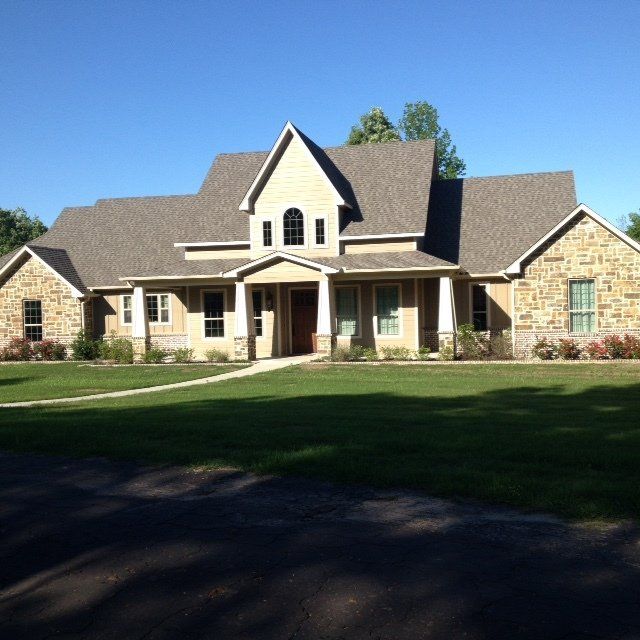 A large house with a gray roof sits on a lush green lawn