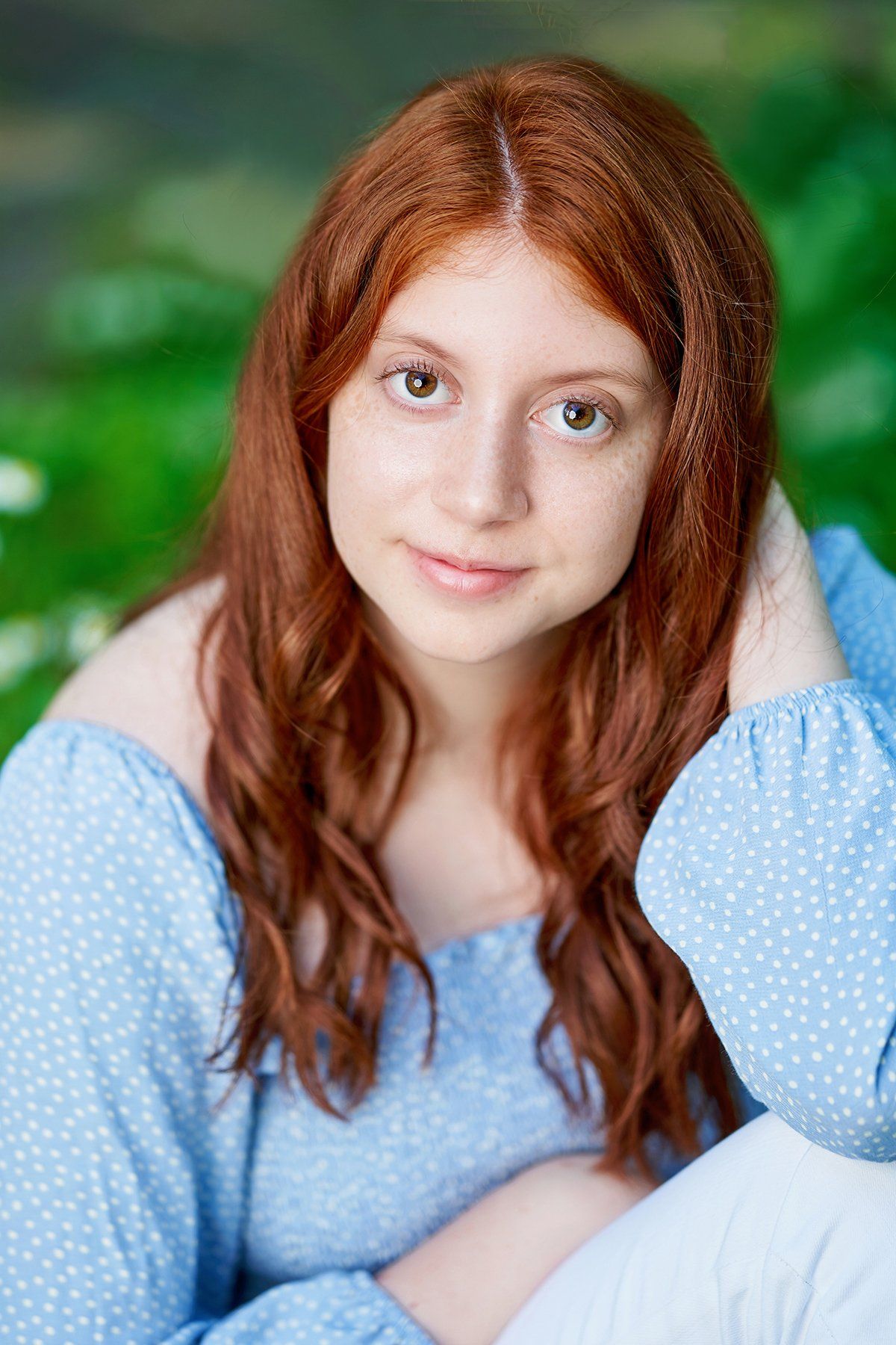 A young woman with red hair is wearing a blue polka dot shirt and white pants.