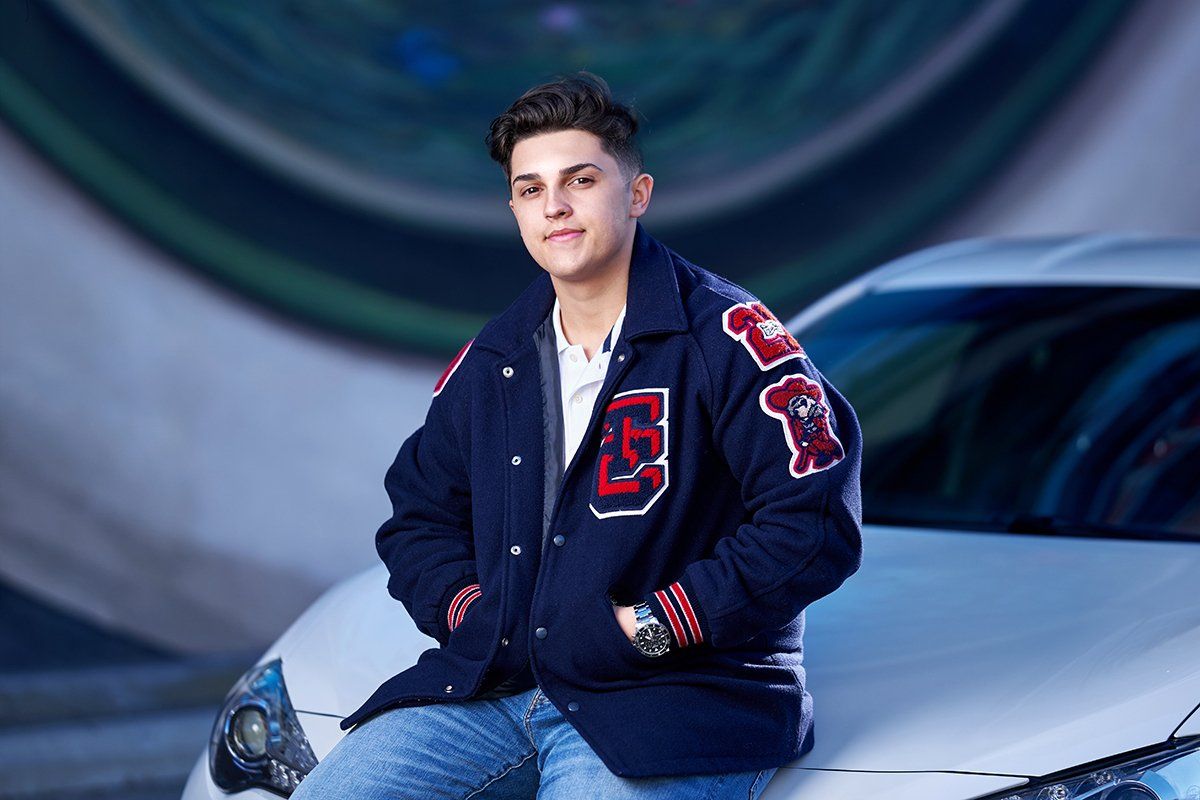 A young man is sitting on the hood of a white car.