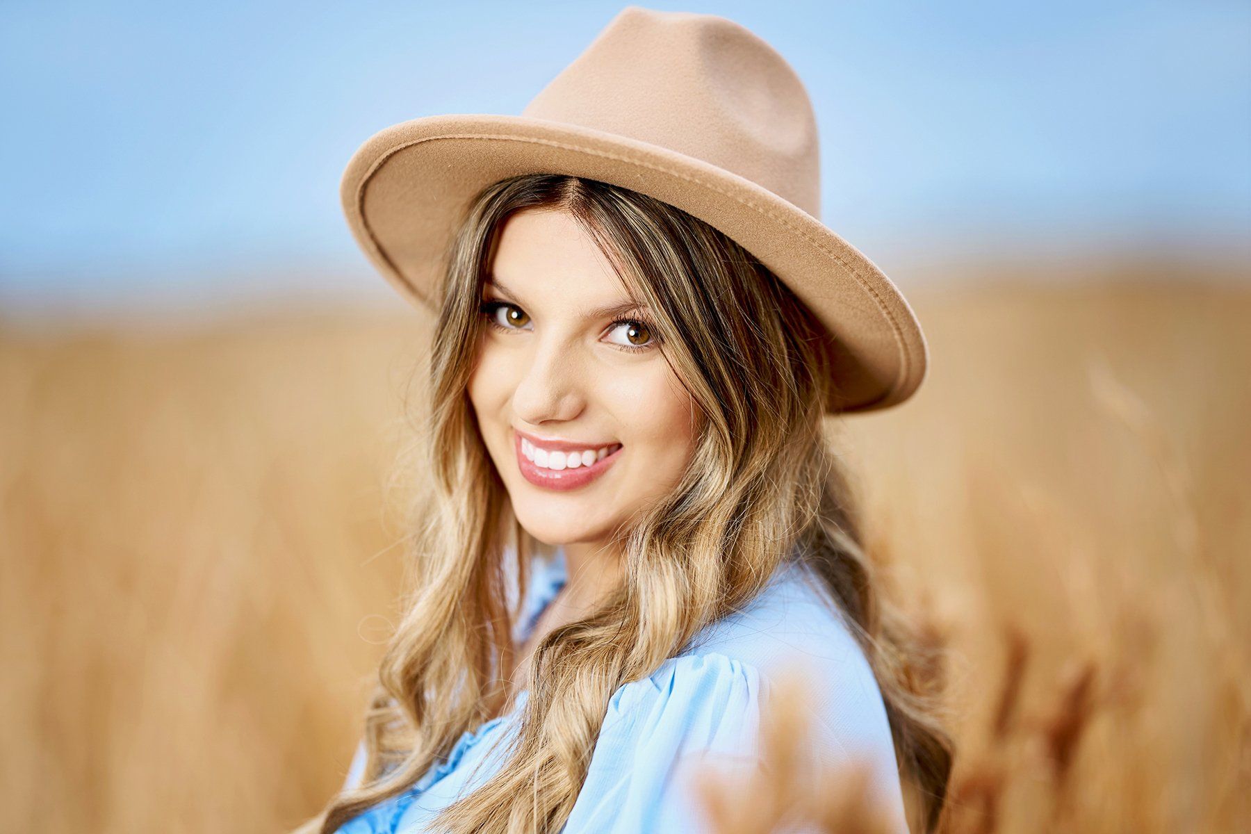 A woman wearing a hat and a blue shirt is standing in a field of wheat.