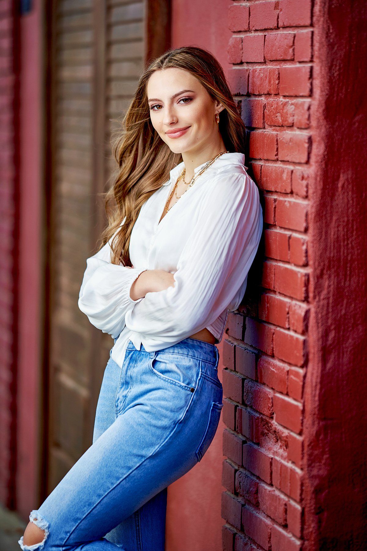 A woman is leaning against a red brick wall with her arms crossed.