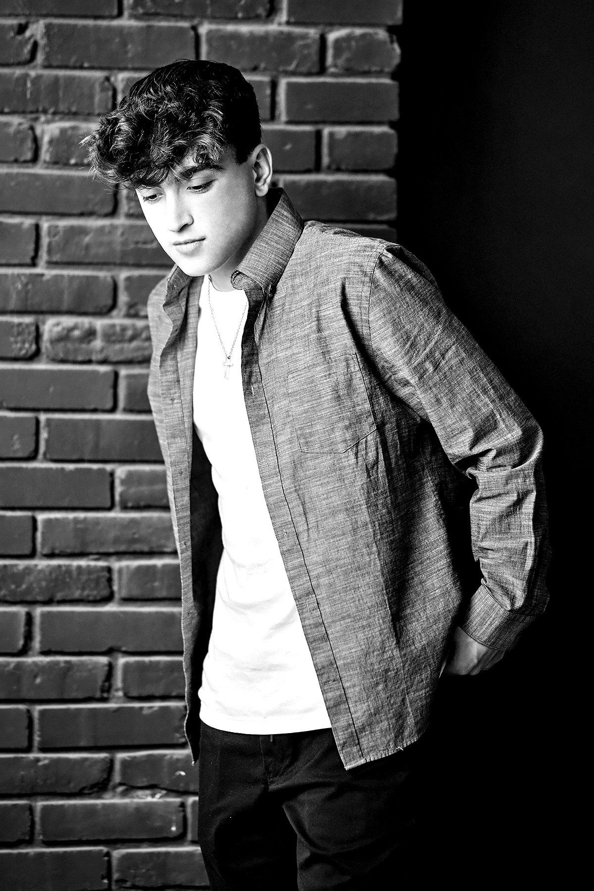 A black and white photo of a young man standing in front of a brick wall.