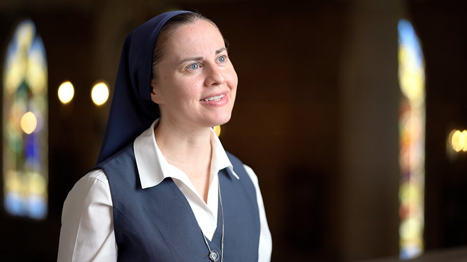 A nun is standing in front of a stained glass window in a church.