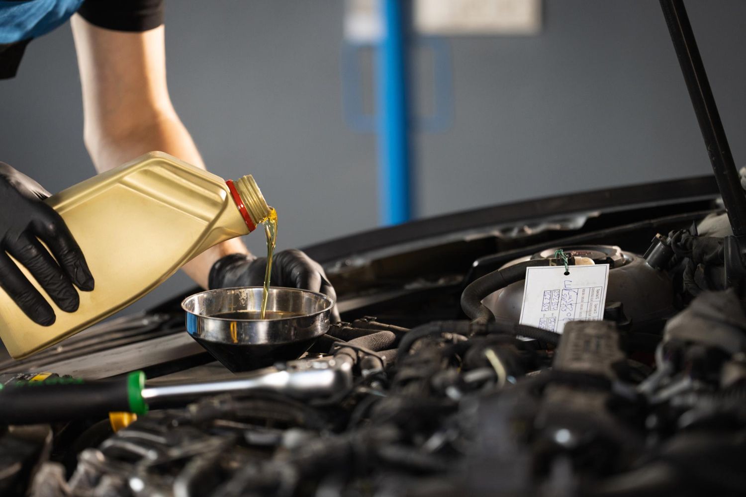 Mechanic pouring oil into a car engine during an oil change, in a garage.