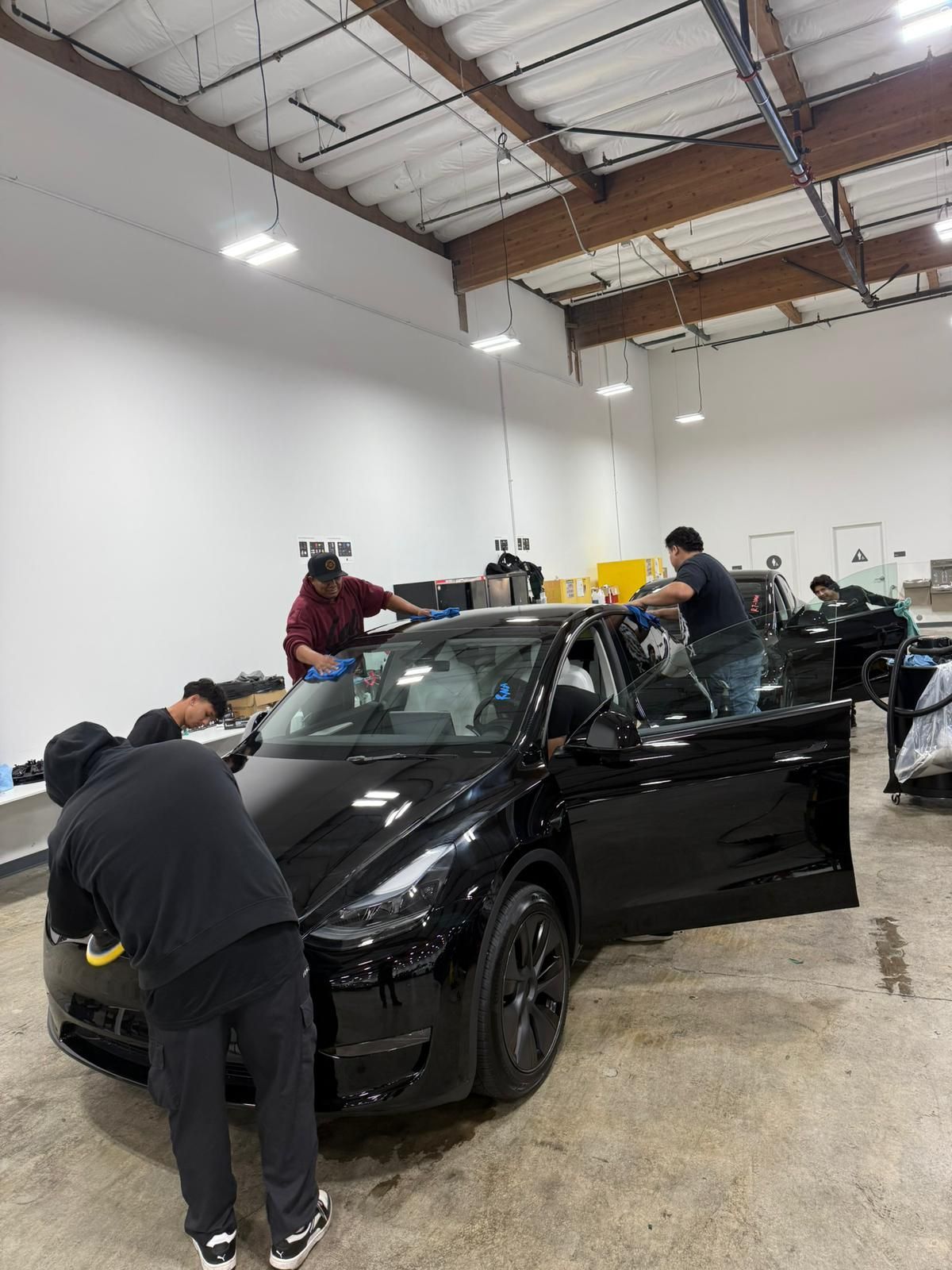 People working on a black car in a white-walled garage.