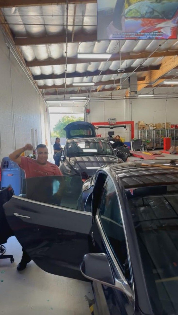 Man poses next to black car with open door in garage; another car is in the background.