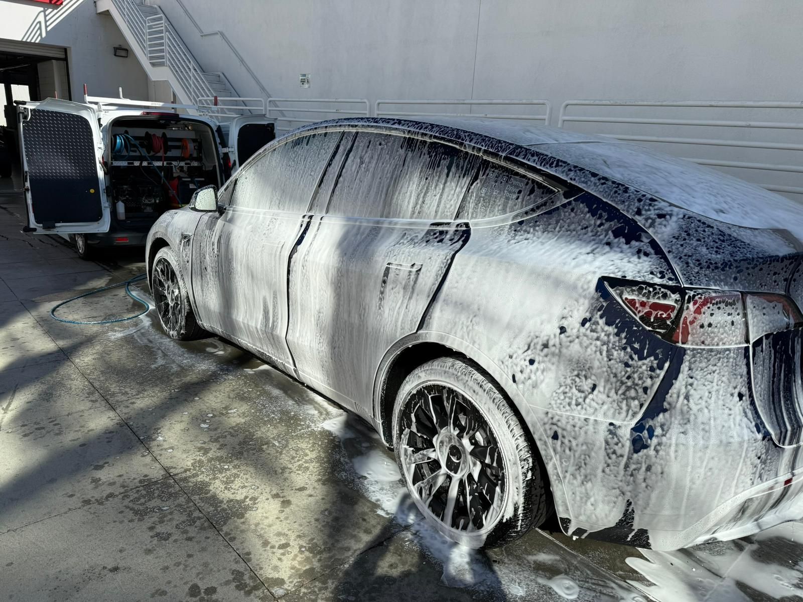 A Tesla car covered in white foam being washed outdoors.
