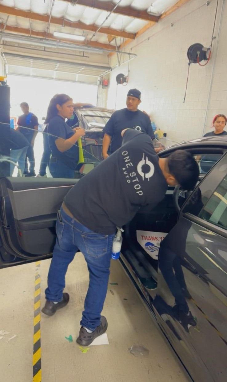 People applying tint to a car window inside a shop.