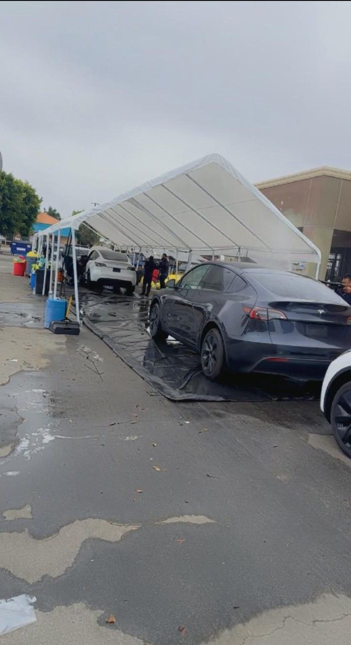 Car wash with black and white cars under a white canopy on a wet, gray day.