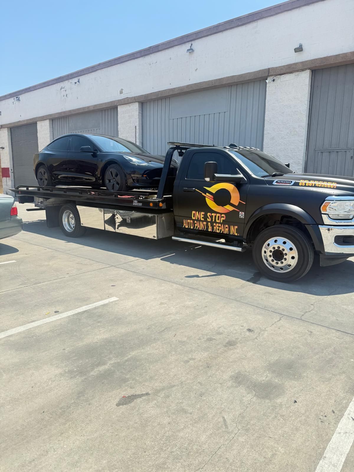 Black car being towed by a black tow truck in front of a building with garage doors.
