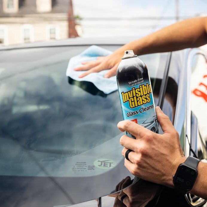 Person spraying and wiping car windshield with 