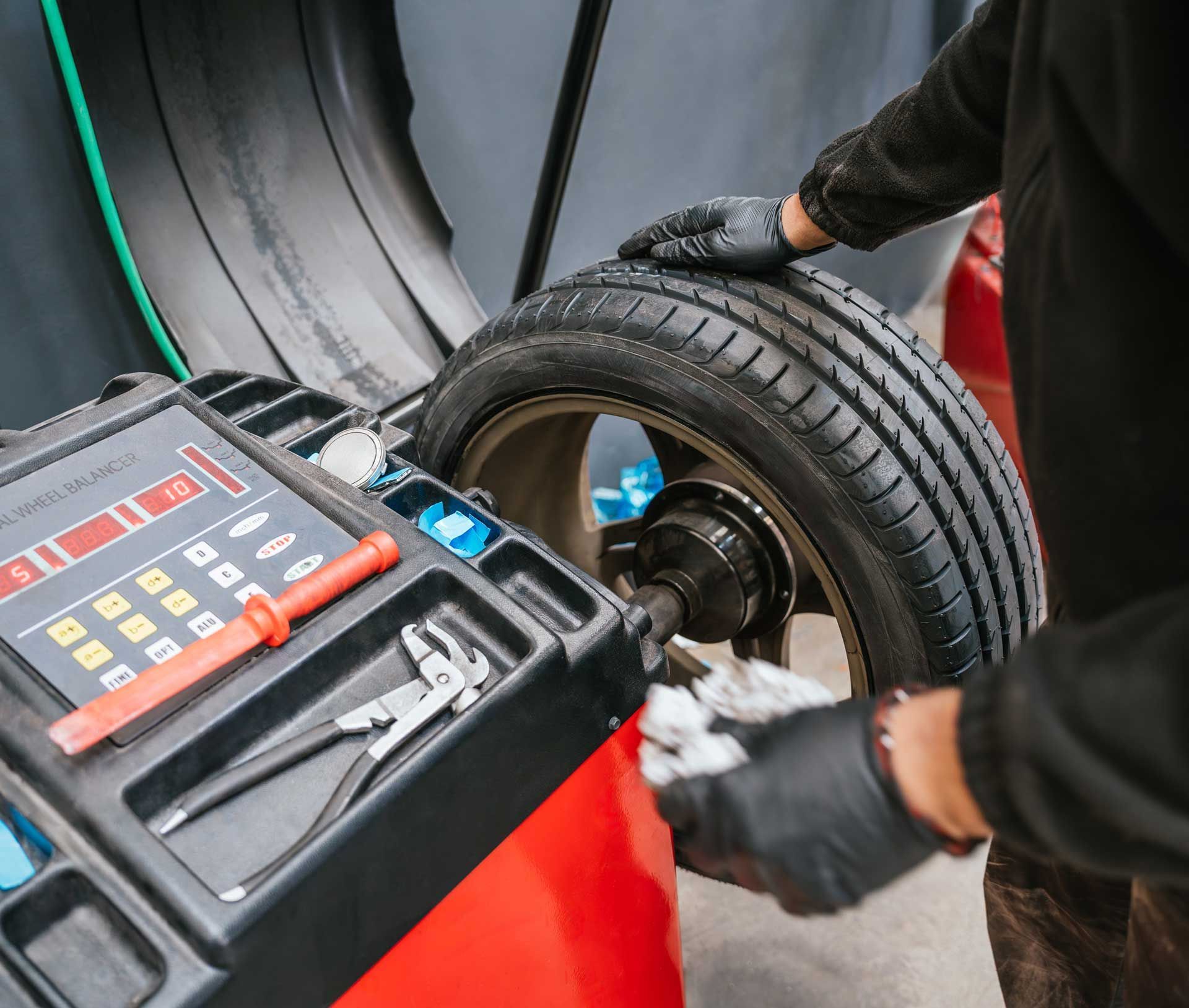 A mechanic balances a car tire on a machine, wearing black gloves.
