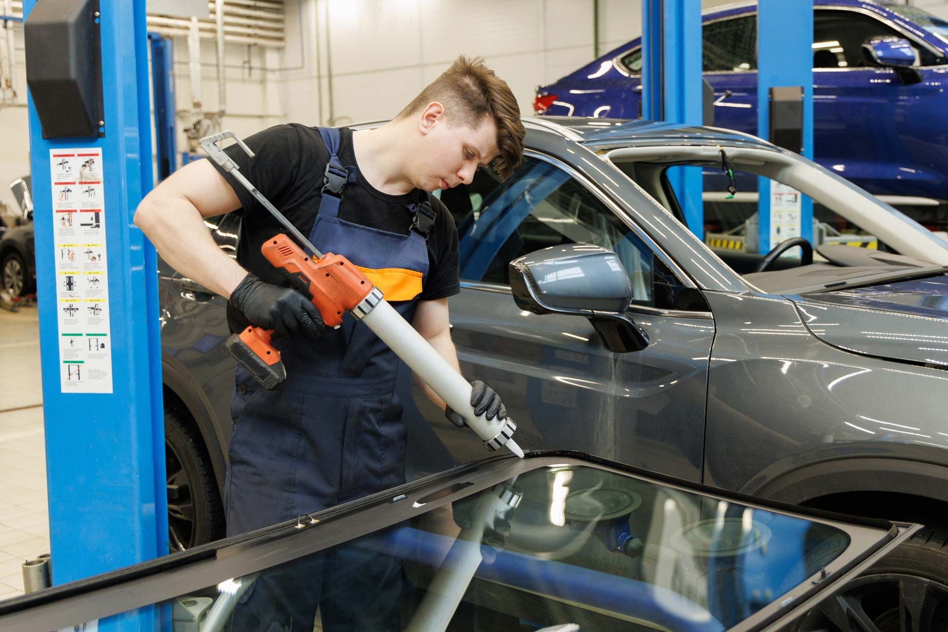 Mechanic applying sealant to a car window in a garage.