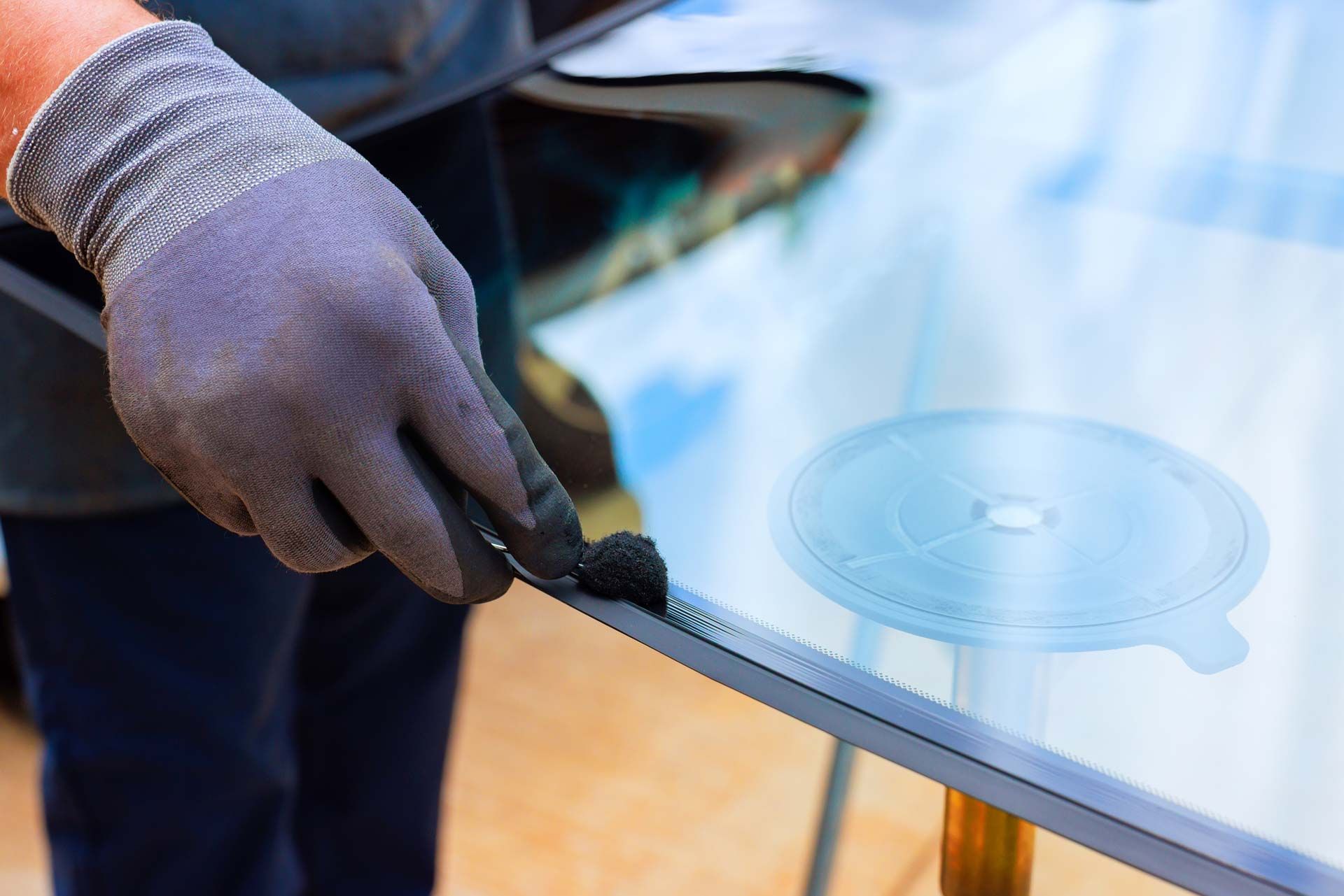 Gloved hand using a tool to apply sealant to a car windshield.