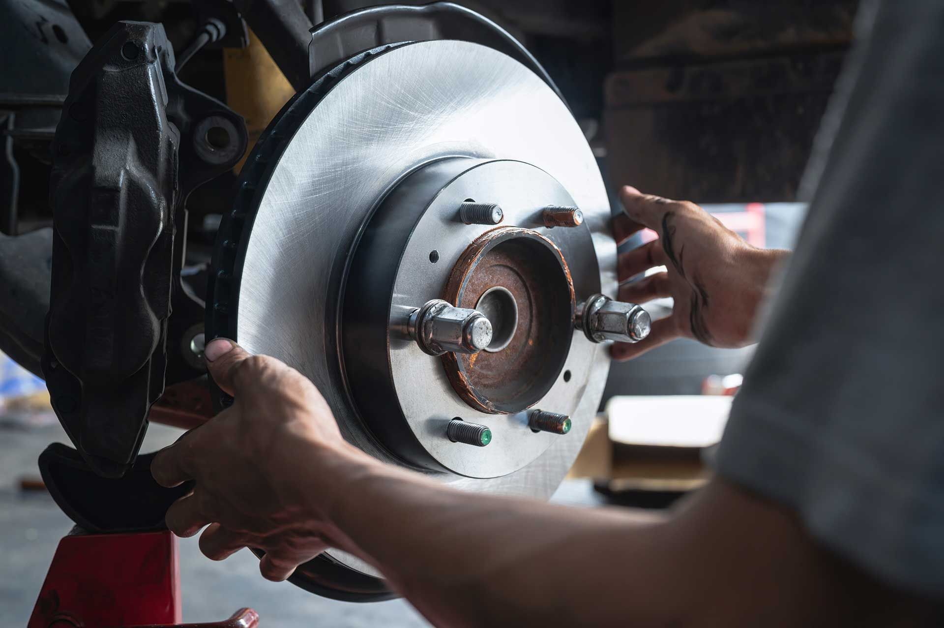 Hands installing a new brake rotor on a car's wheel hub in a garage.