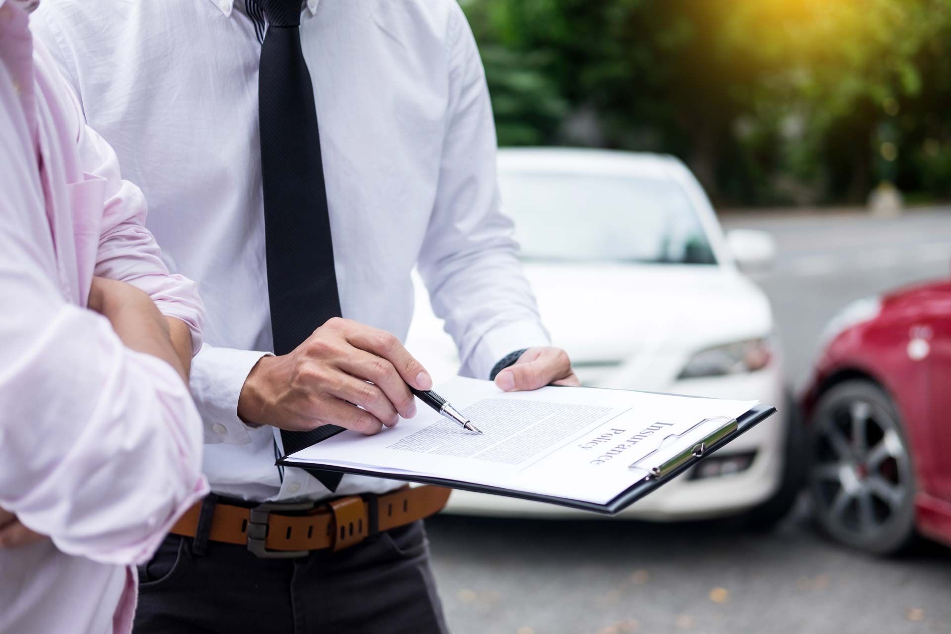 Person in a suit reviews a document with another person near damaged cars.