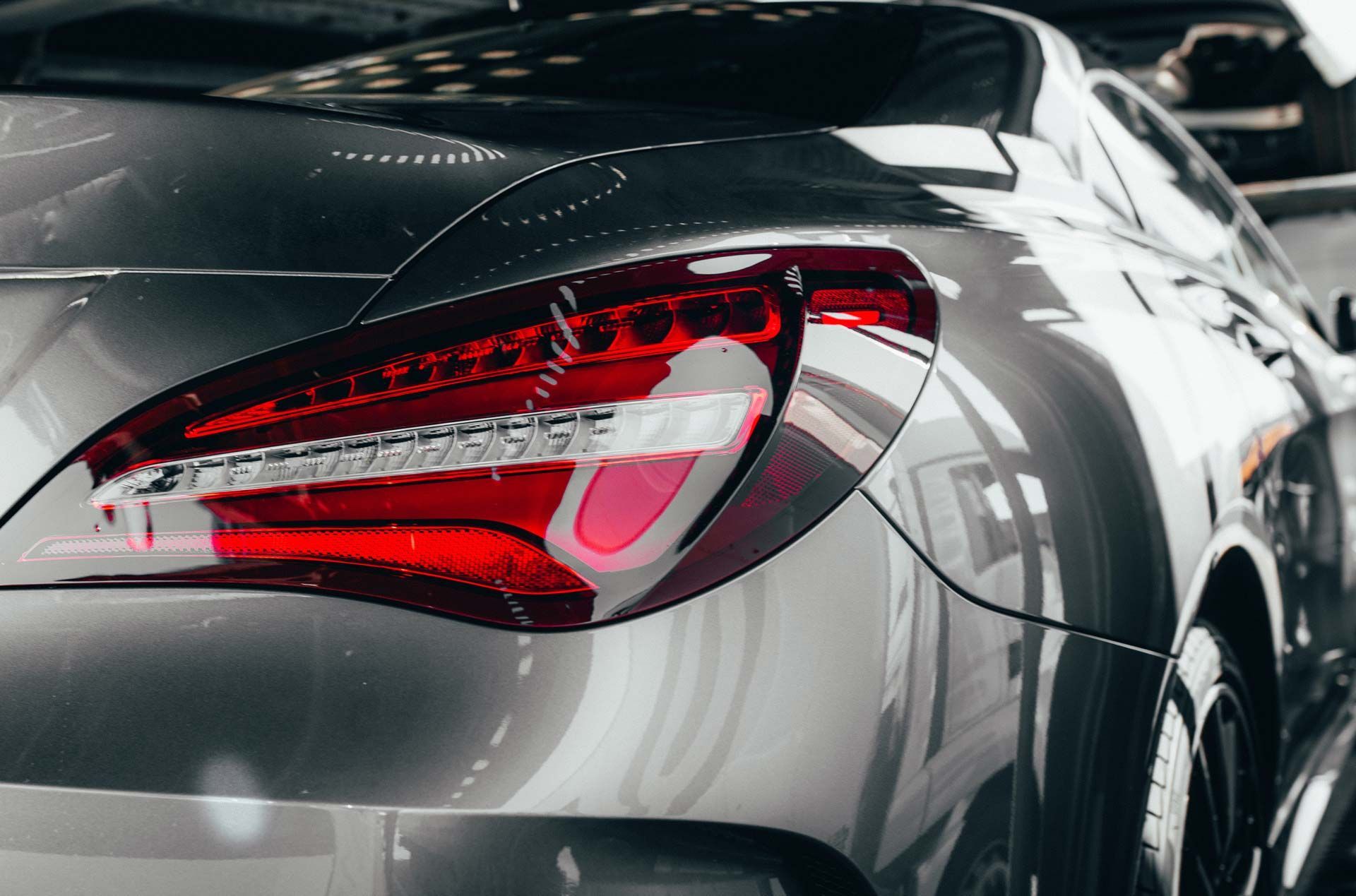 Gray car's rear, taillight illuminated in red and pink.