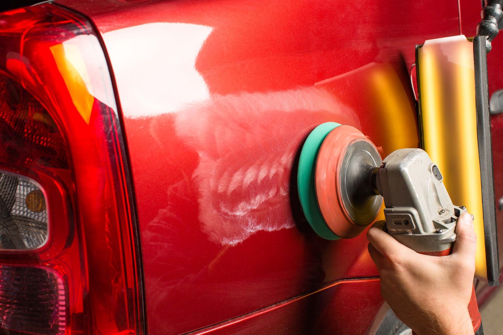 Person using a power buffer on a red car, creating swirl marks on the paint.