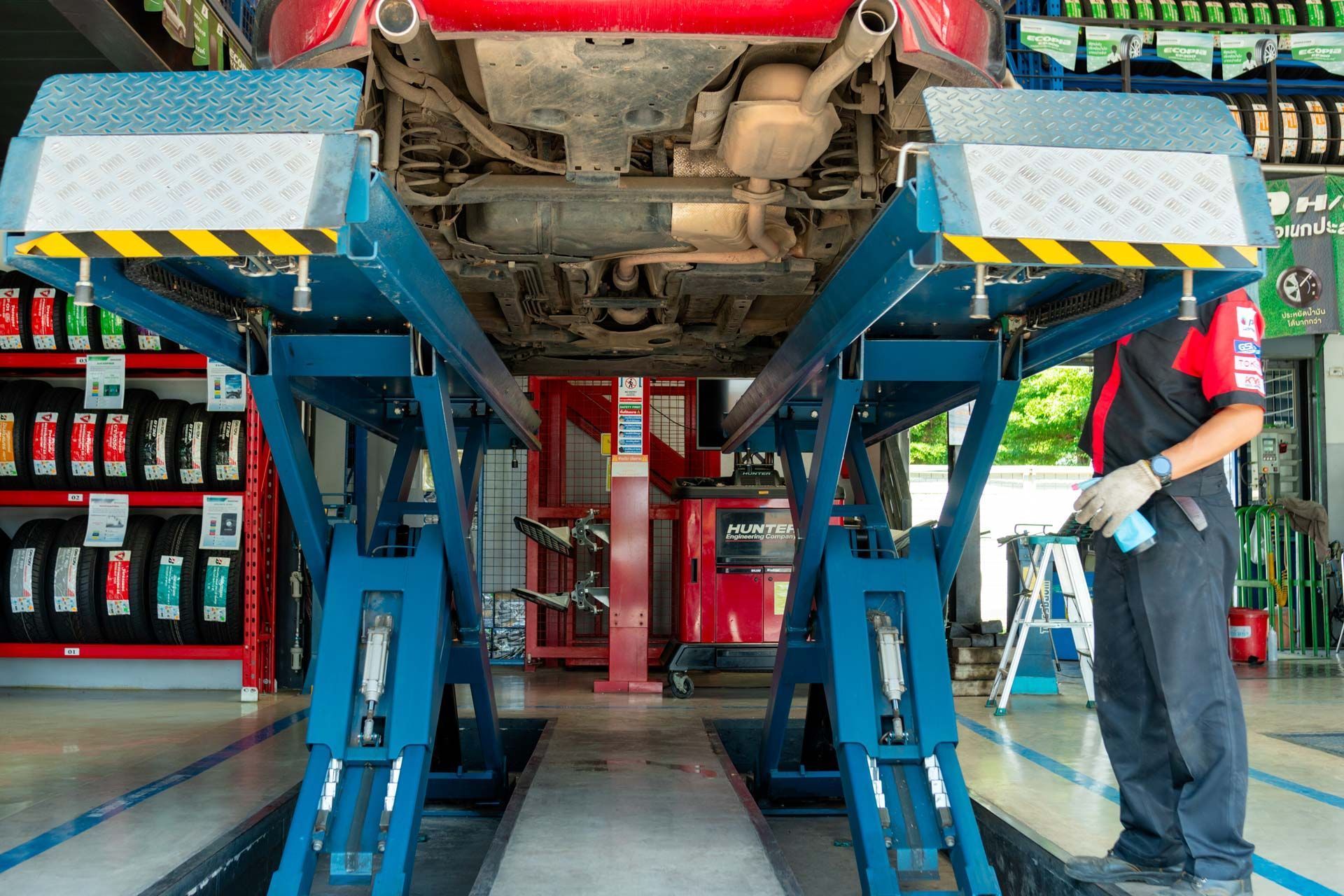 Car on a blue lift in a garage; a mechanic stands nearby.