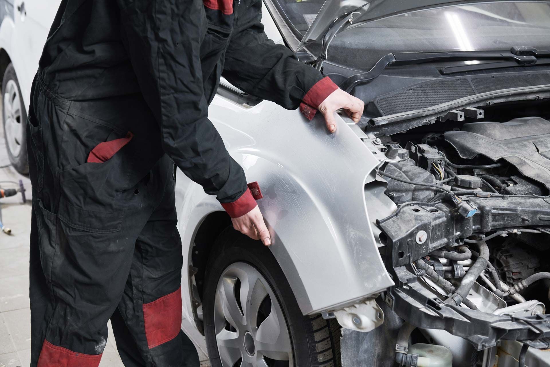 Mechanic in black and red overalls installing a car fender.