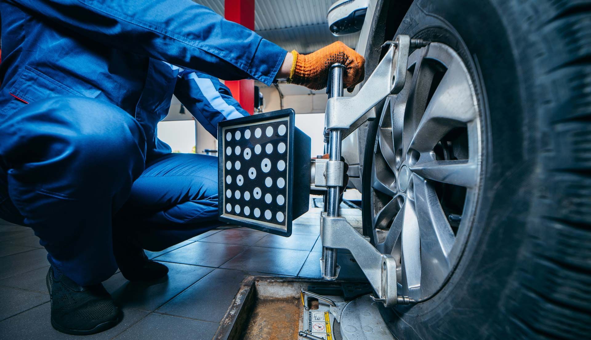 Mechanic adjusting wheel alignment, using a tool on a car tire in a garage.