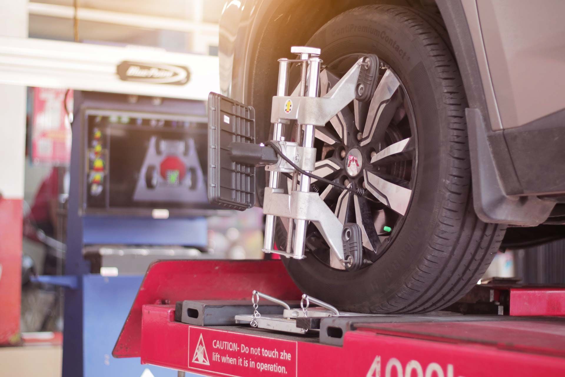 Car tire on lift during wheel alignment; equipment attached to tire, digital display in background.