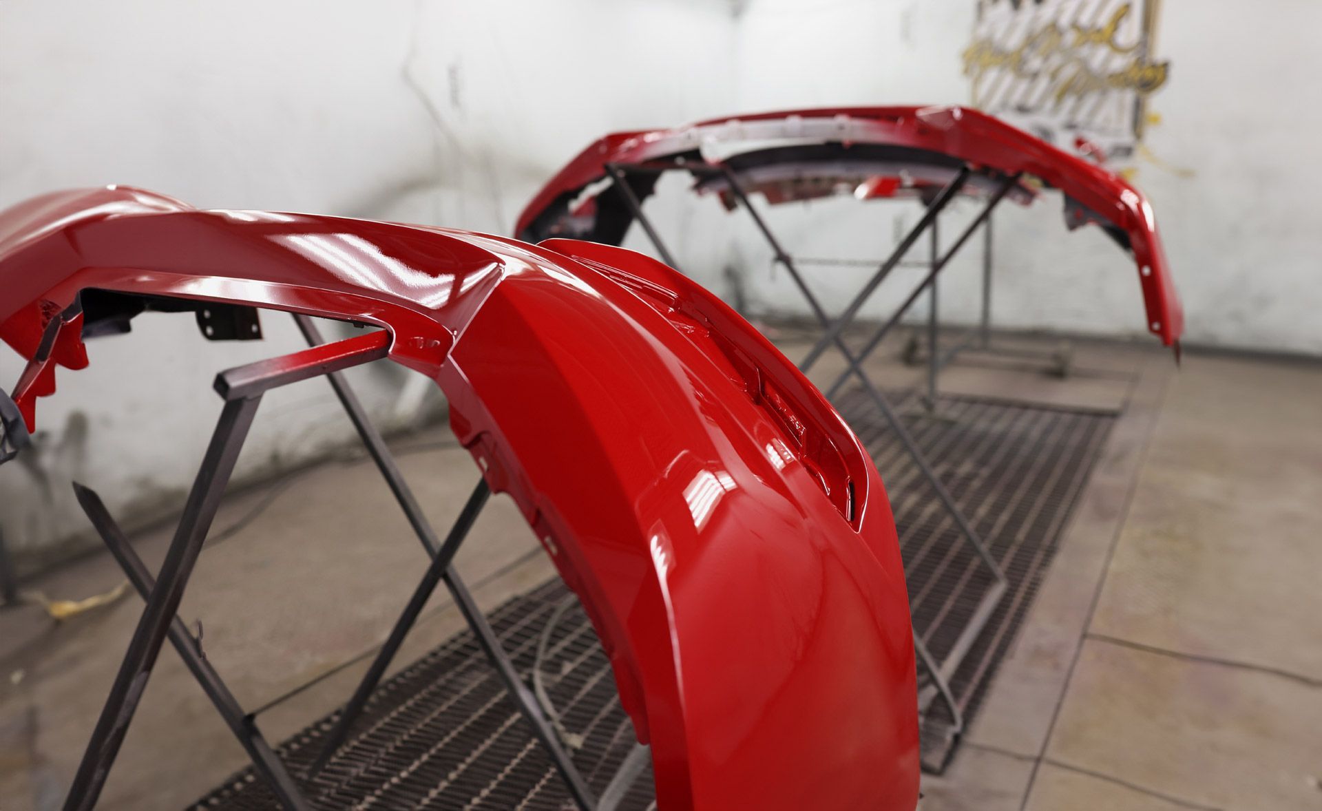 Two red car bumpers on stands in a spray painting booth.