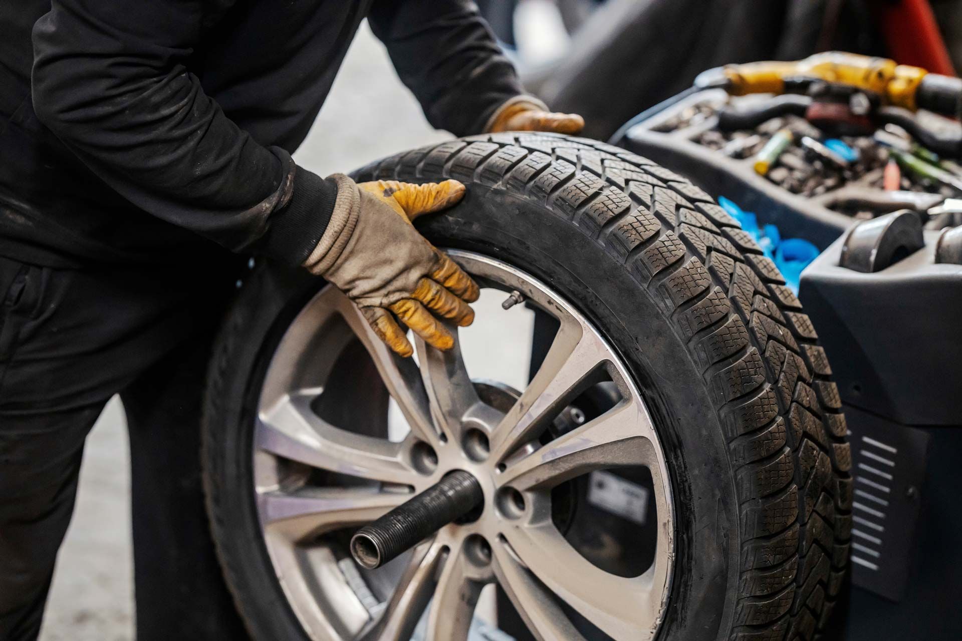 Person in gloves balancing a tire on a machine in a garage.