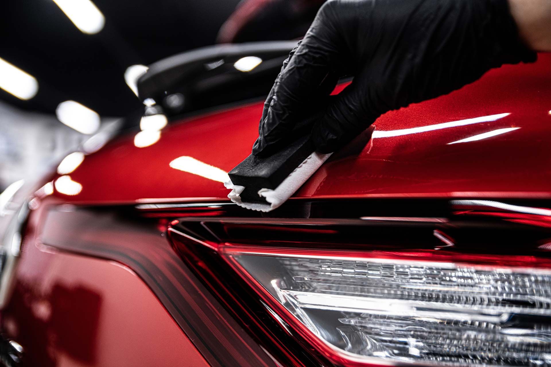 Black-gloved hand applying ceramic coating to a red car's body panel with a white applicator.