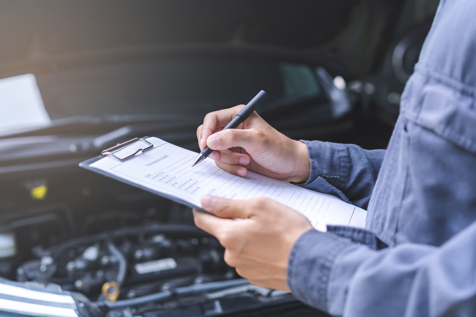 Mechanic writing on a clipboard while inspecting a car engine.