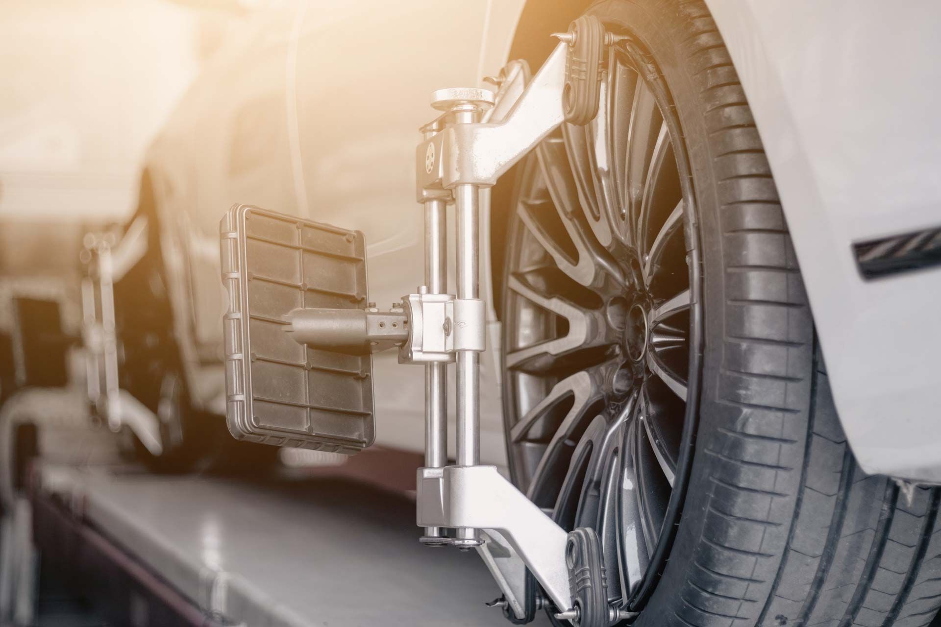 Car tire being aligned on a lift with a wheel alignment machine attached, indoors.