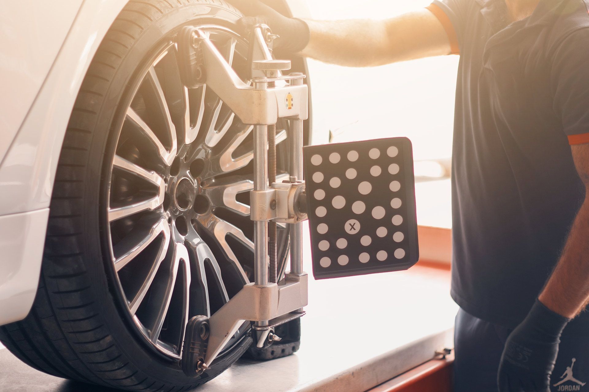A mechanic using wheel alignment equipment on a car tire in a garage.