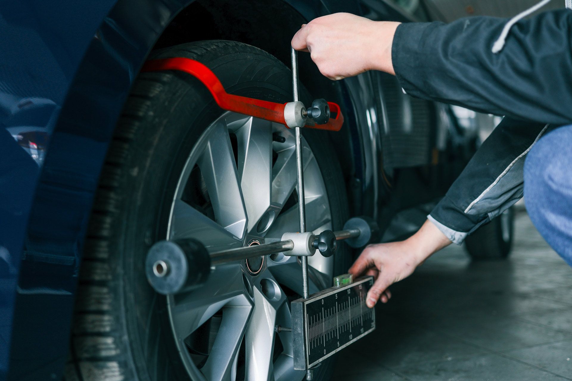 Car wheel being aligned by a mechanic using a measuring tool in a garage.