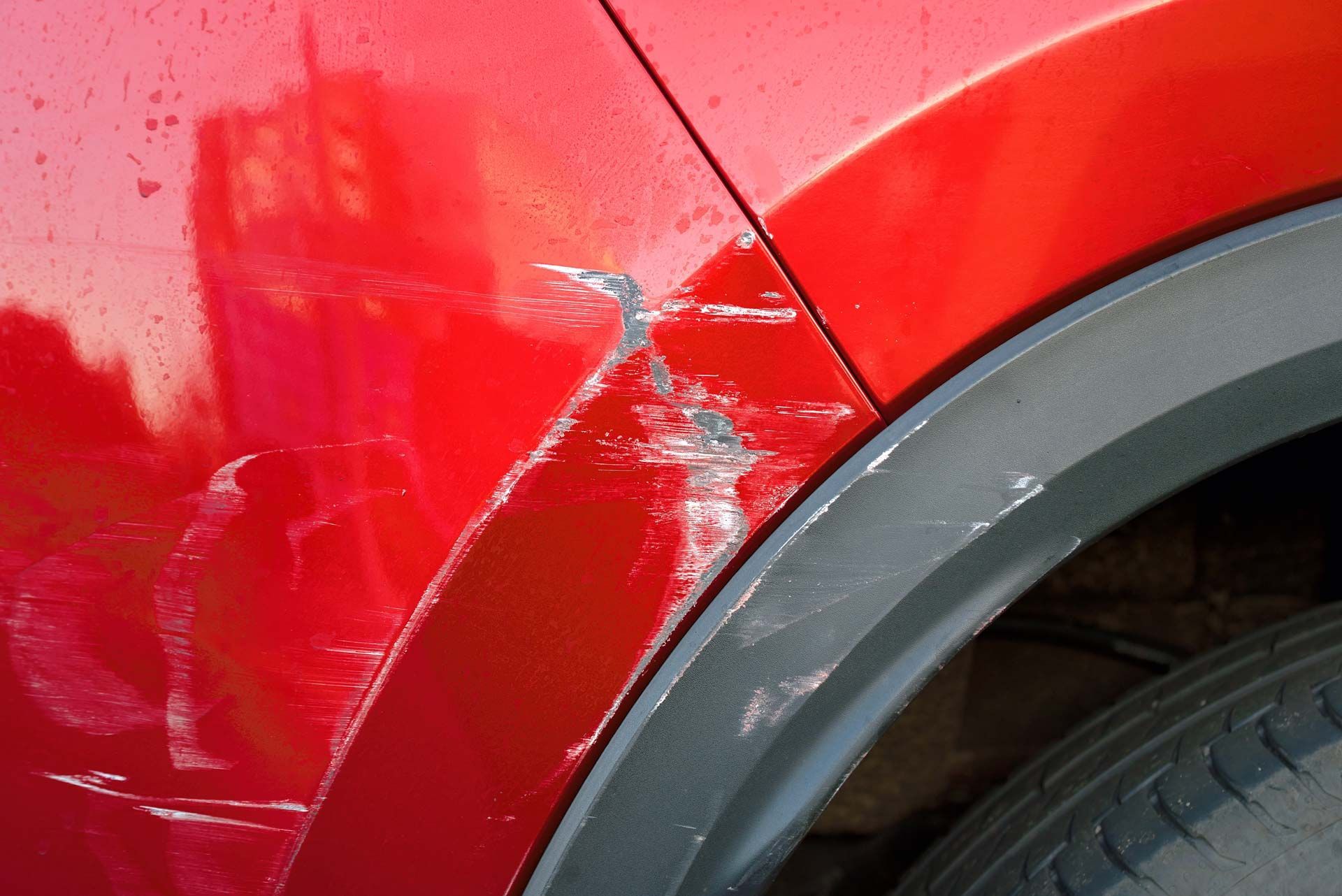 Red car with paint scratches and damage near the wheel well.
