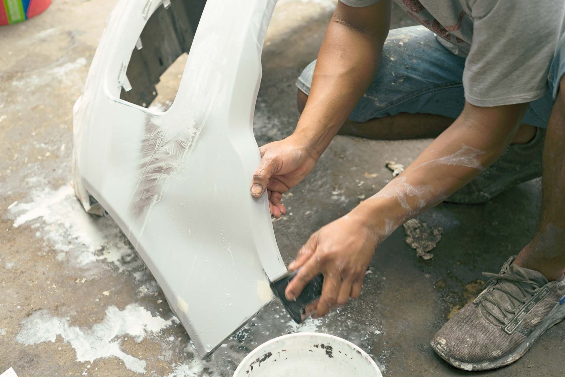 Person using a putty knife to smooth filler on a car bumper, likely for repair.