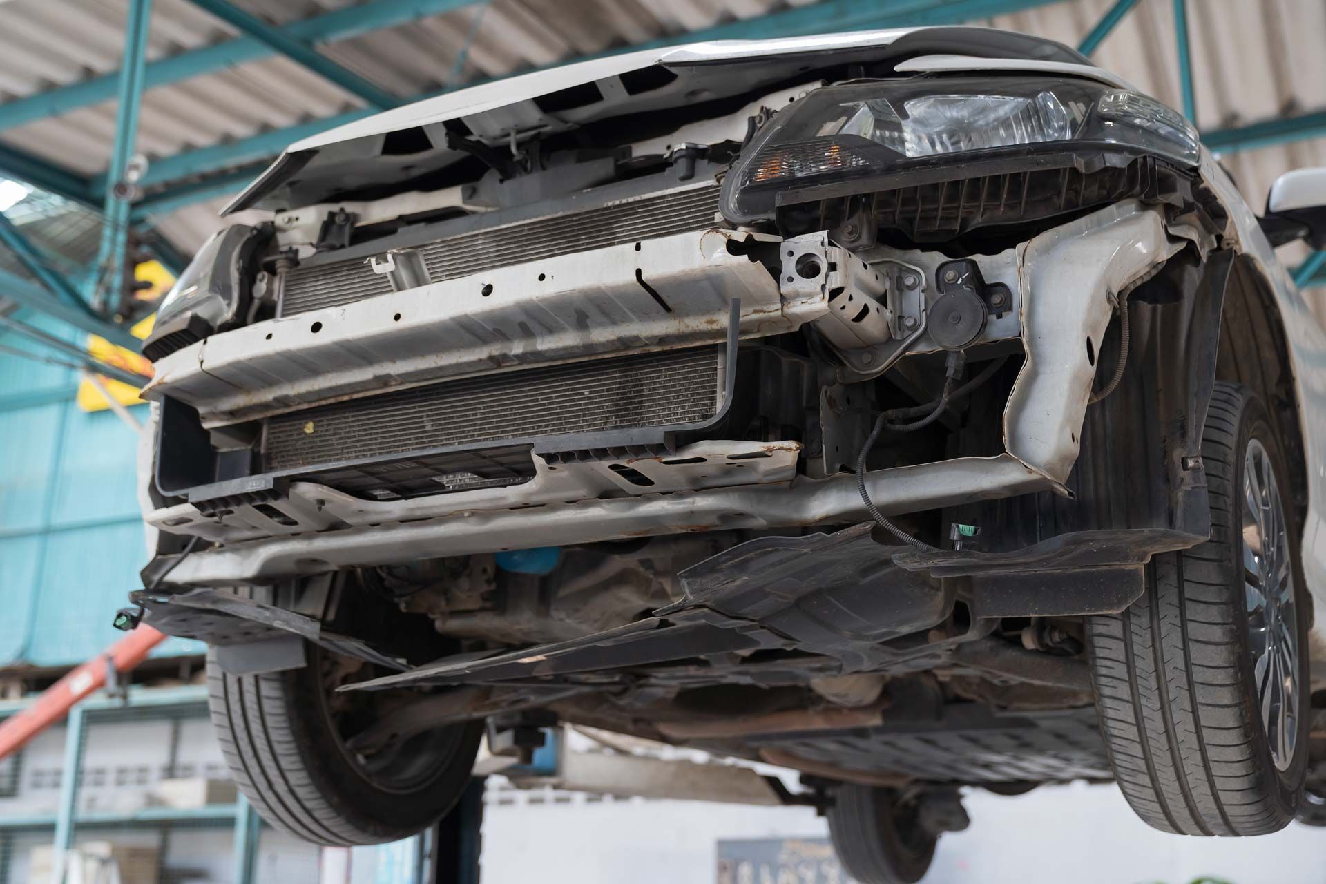 Car with damaged front end, raised on a lift in a repair shop.