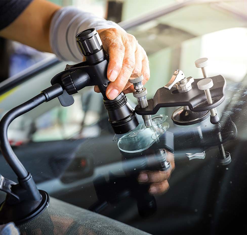 Person repairing windshield crack with specialized tools.