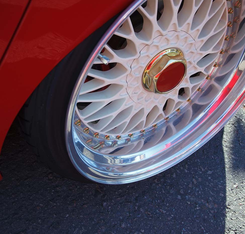 Close-up of a red car wheel with a white, intricate spoke design and a chrome rim.