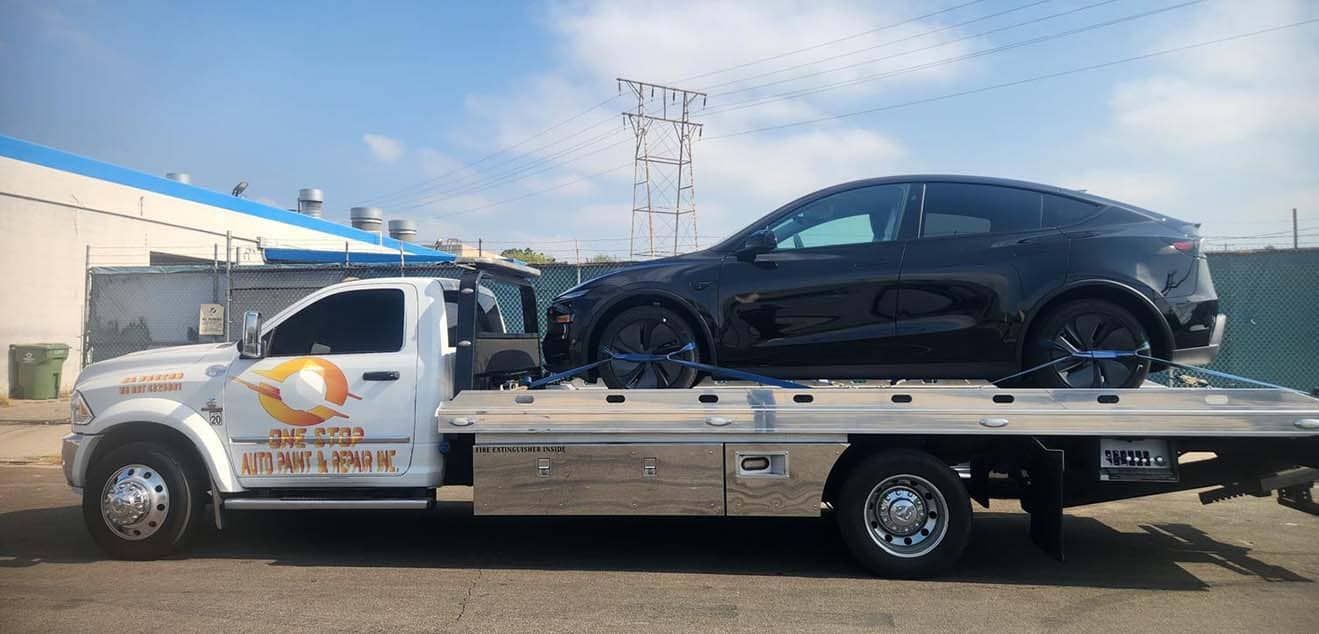 Black car on a tow truck. White truck has logo. Bright sunny day.