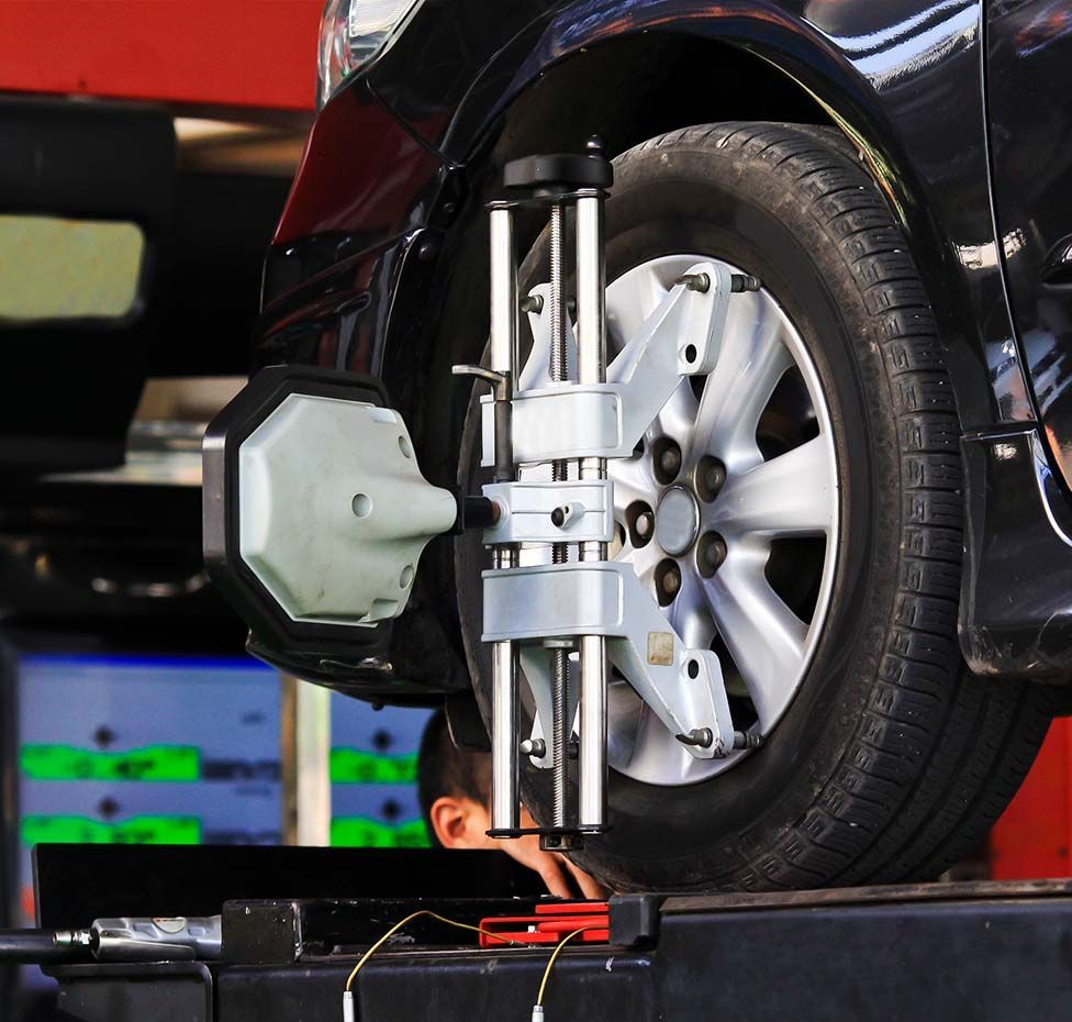 Car tire undergoing alignment check at a service station, with a mechanic inspecting it.