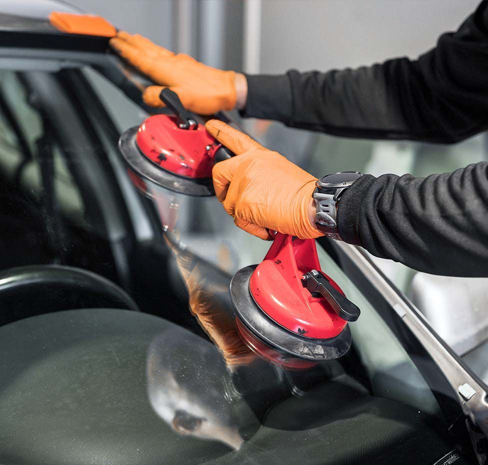 Person in orange gloves uses suction cups to remove a car windshield.
