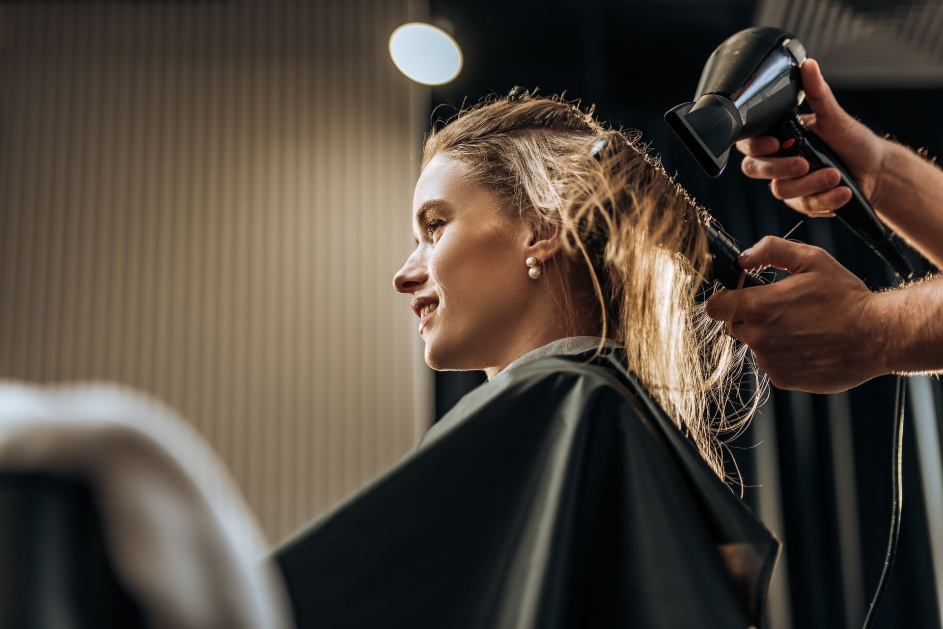 Woman smiling at a salon as a stylist uses a hairdryer on her wet hair