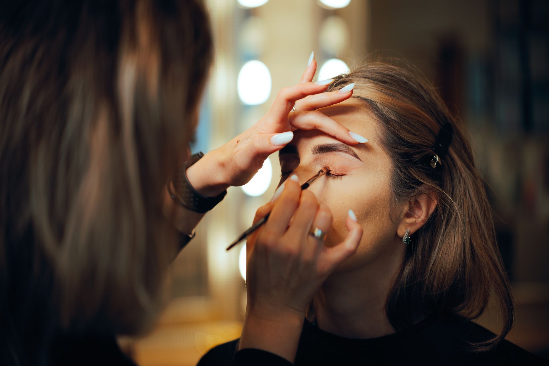 Woman having eye makeup applied in front of a mirror with lights
