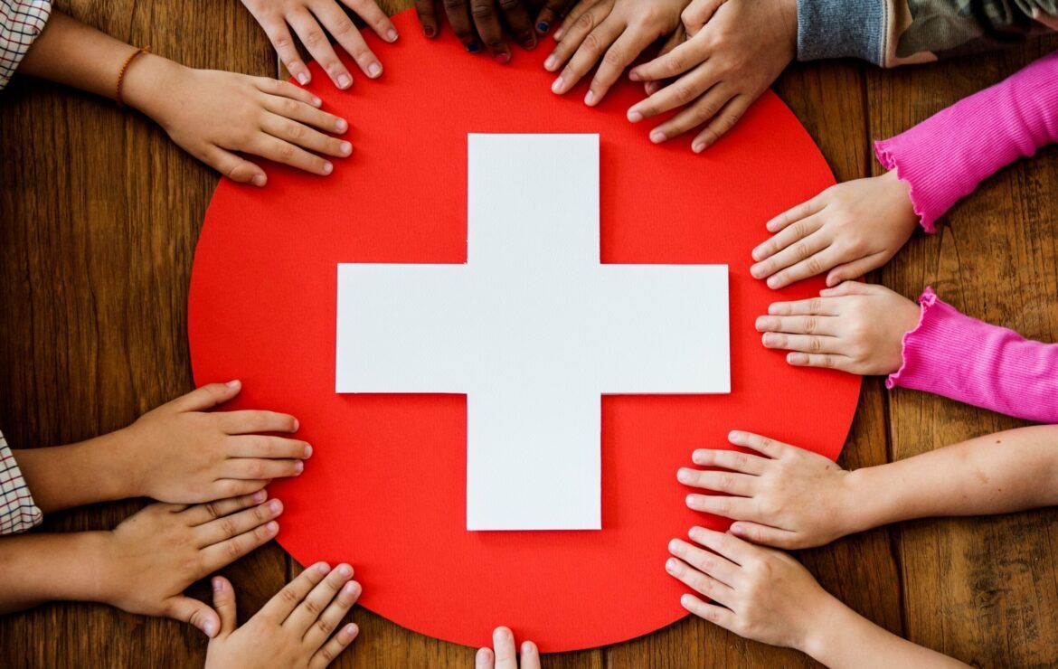 A group of children are holding a red circle with a white cross on it.