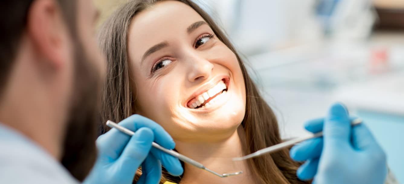 A woman is smiling while having her teeth examined by a dentist.