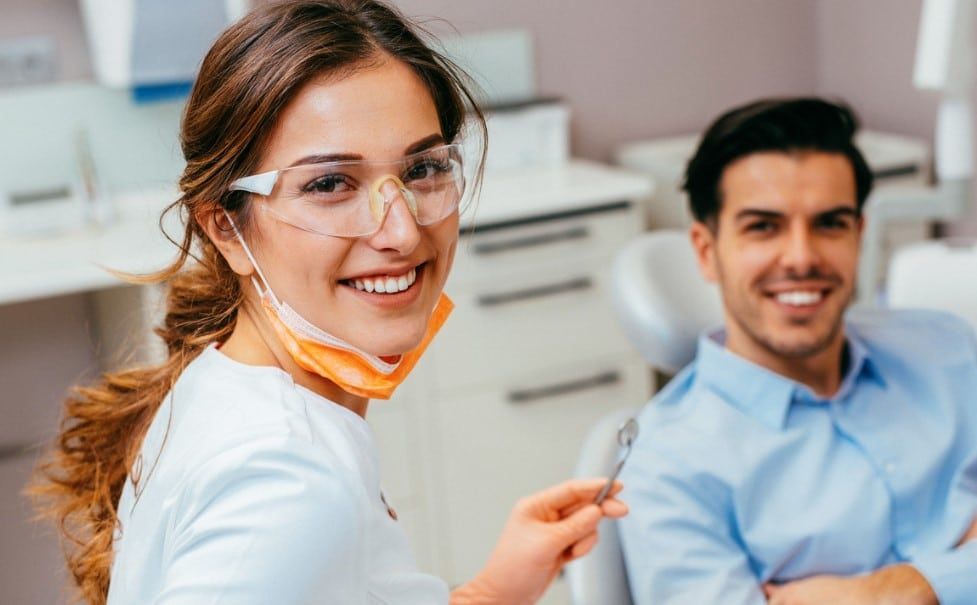 A woman is holding a toothbrush in front of a man in a dental chair.